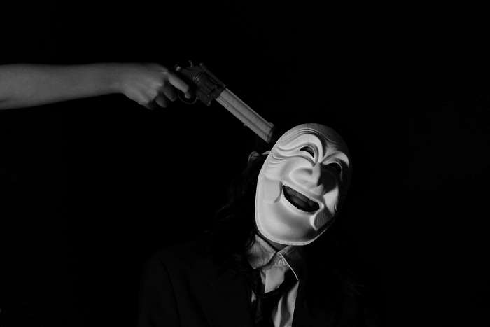 Hand holding gun to masked person's head
