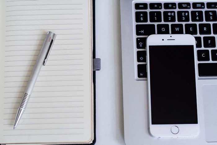 Apple laptop with iPhone, notebook, and pen