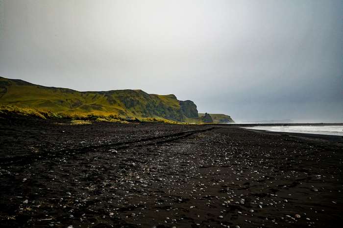 Black sand beach with green hills and cloudy sky