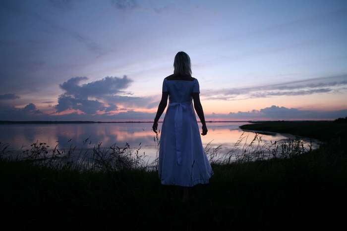 Woman in white dress by the water at dusk