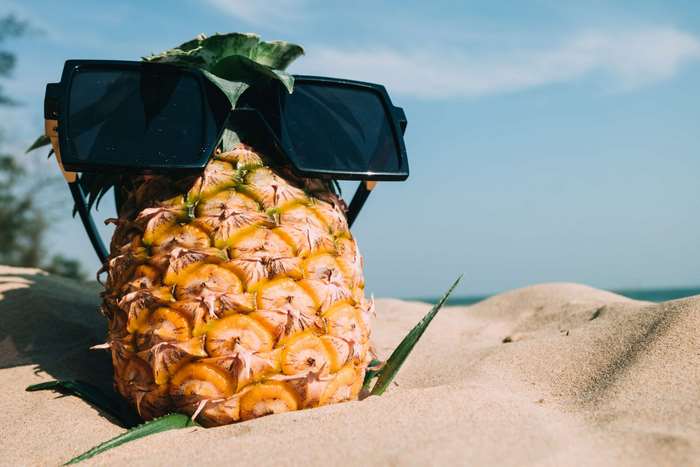 Pineapple with sunglasses on a sandy beach