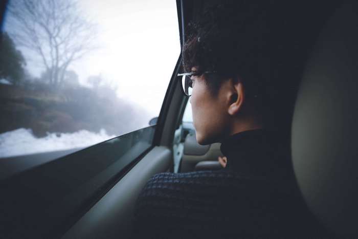 Person wearing glasses looking out car window in winter fog