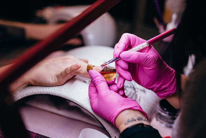 Manicurist applying nail extension with brush and form