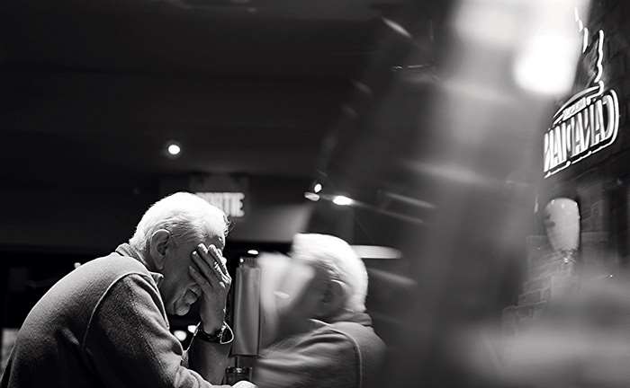 Elderly man with hand over face in black and white