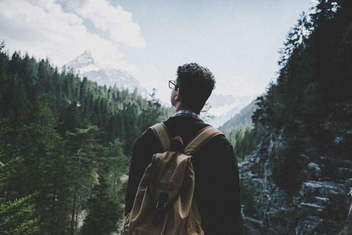 Man with backpack looking at mountains in forest