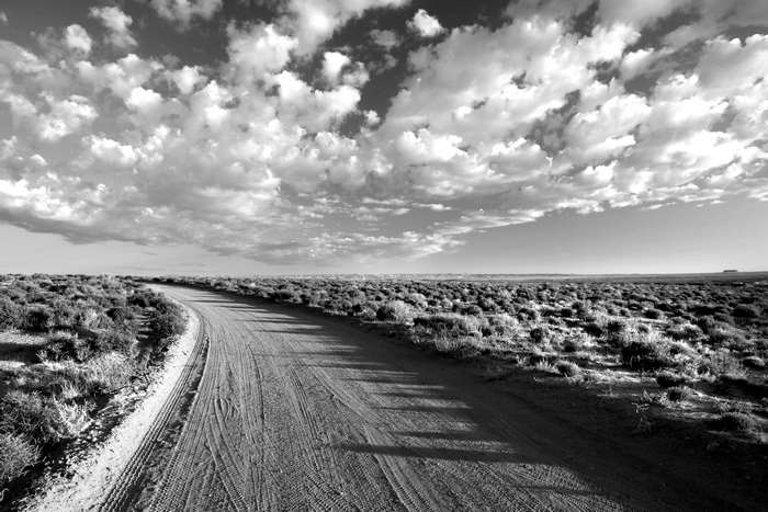 Dirt road through arid landscape with clouds