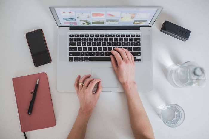 Hands typing on a laptop with smartphone and notebook