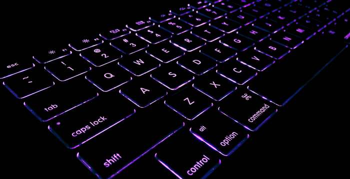 Backlit Apple MacBook keyboard with purple glow