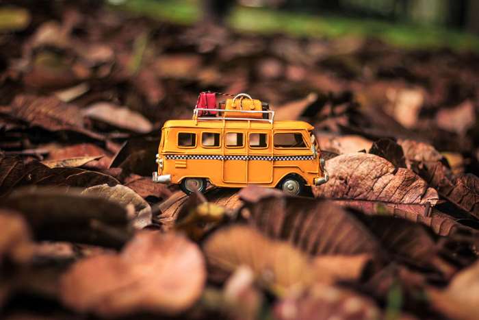 Orange toy van with luggage on roof on fallen leaves
