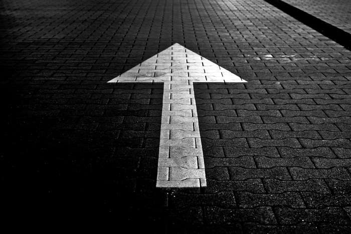 White arrow painted on a dark brick road