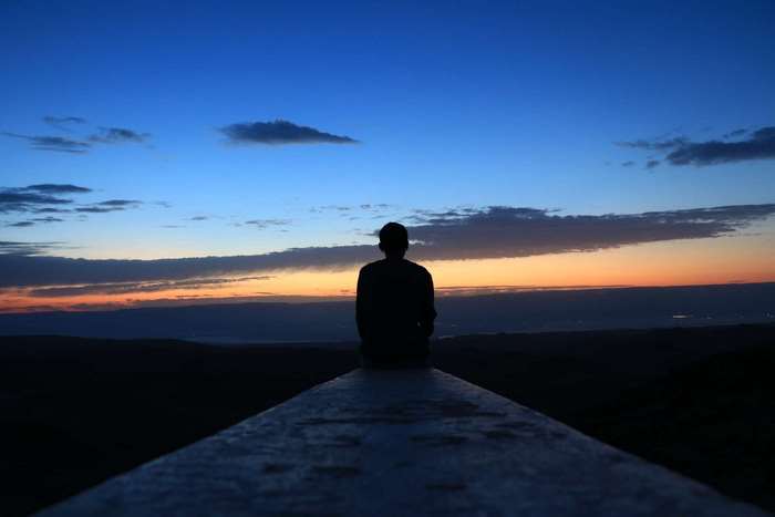 Silhouette of a person sitting on a ledge at sunset