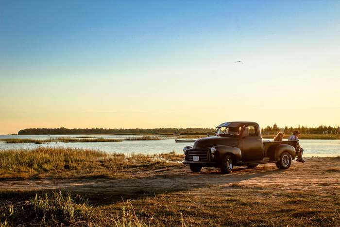 Couple and dog in old truck by lake at sunset