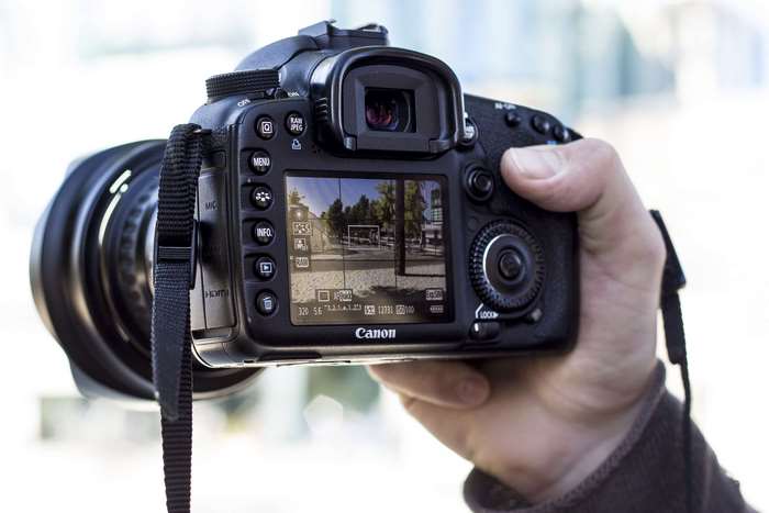 Canon DSLR camera held in hand, showing screen display