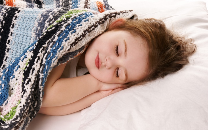 A young girl sleeping peacefully under a colorful blanket