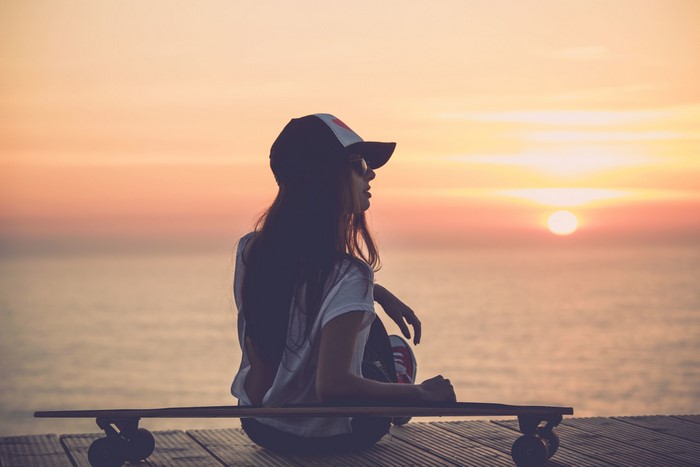 Girl Sitting with Skateboard Watching Sunset by the Sea