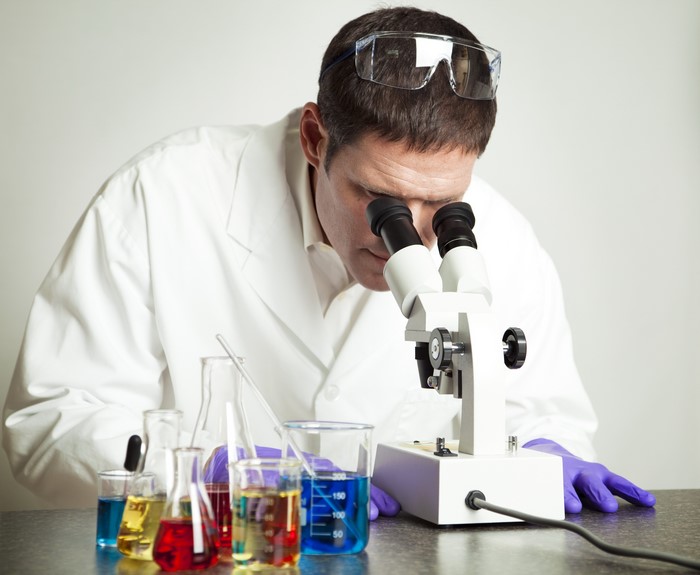 Scientist looking into a microscope with colorful liquids in flasks