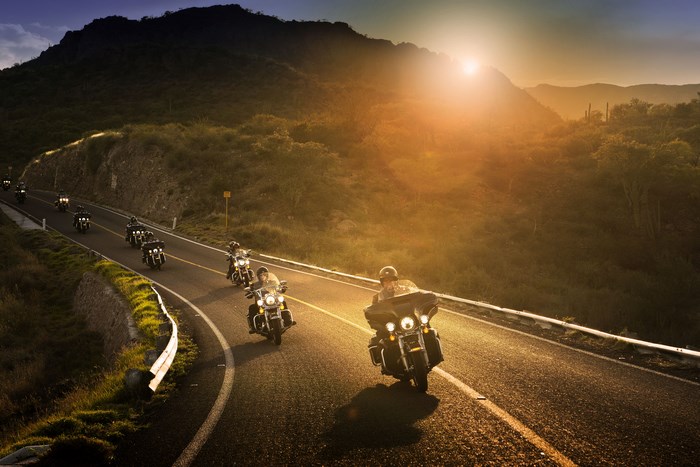 Harley Davidson motorcycles riding on a road at sunset