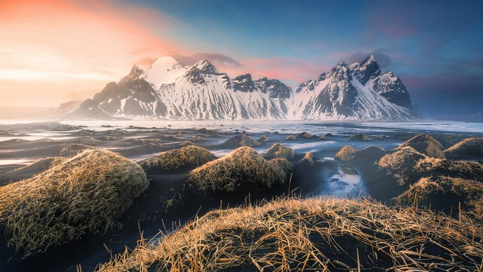 Snow-capped mountains on a black sand beach with dry grass