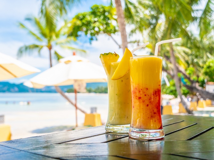 Two tropical fruit smoothies on a table at the beach