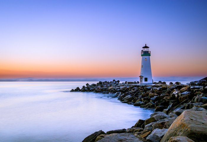 White lighthouse on a rocky shore at sunset