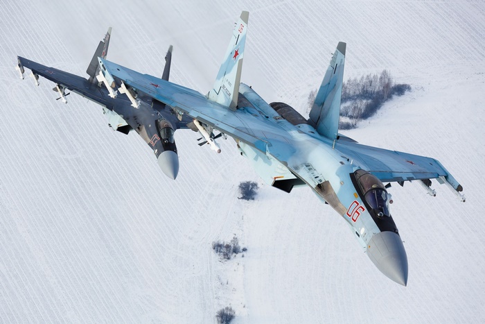 Two Sukhoi Su-35 fighter jets flying over a snowy landscape