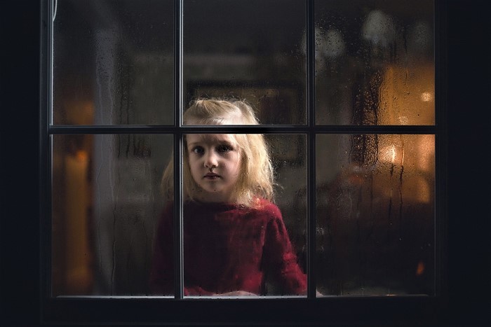 Little girl looking through a rainy window