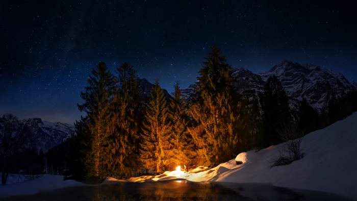 Campfire in snowy mountains under starry night sky