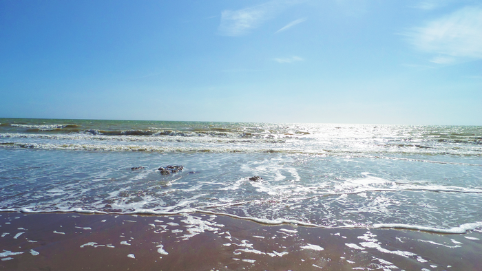 Ocean waves on a sandy beach under a blue sky