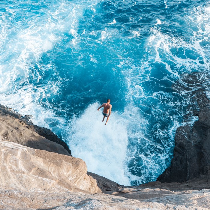 Man jumping off rocky cliff into ocean waves