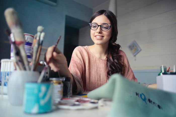 Young woman with glasses painting at a desk