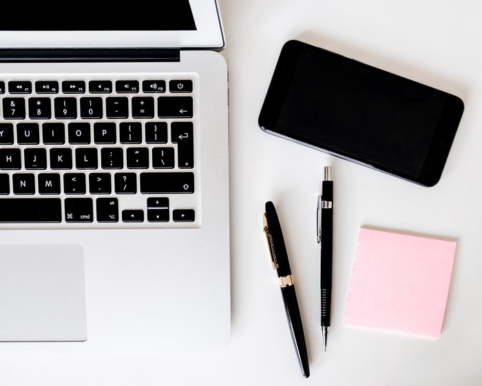 Laptop, smartphone, pens, and sticky note on a desk