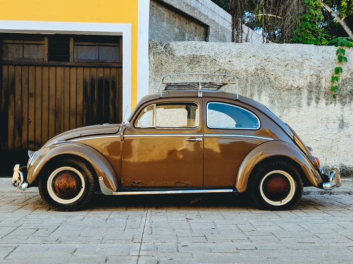 Brown Volkswagen Beetle parked in front of a yellow garage