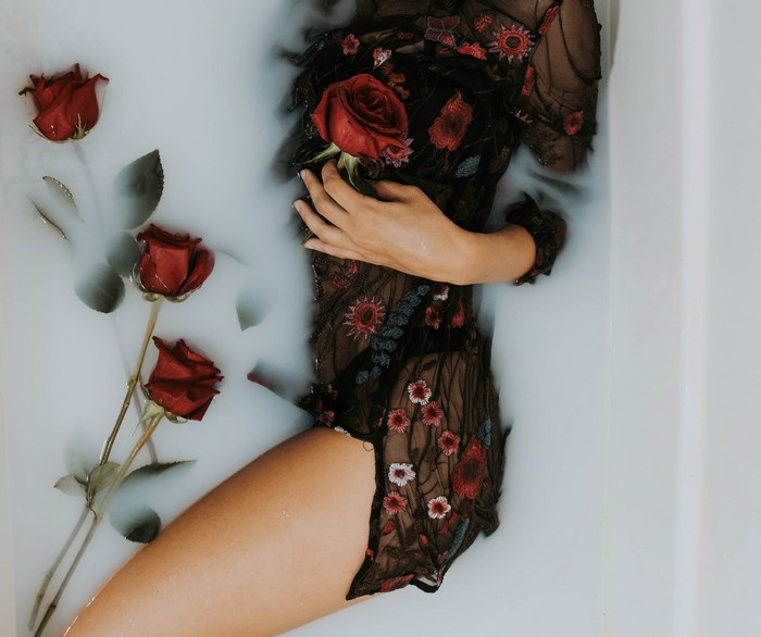 Woman in a black floral dress in a milk bath with roses