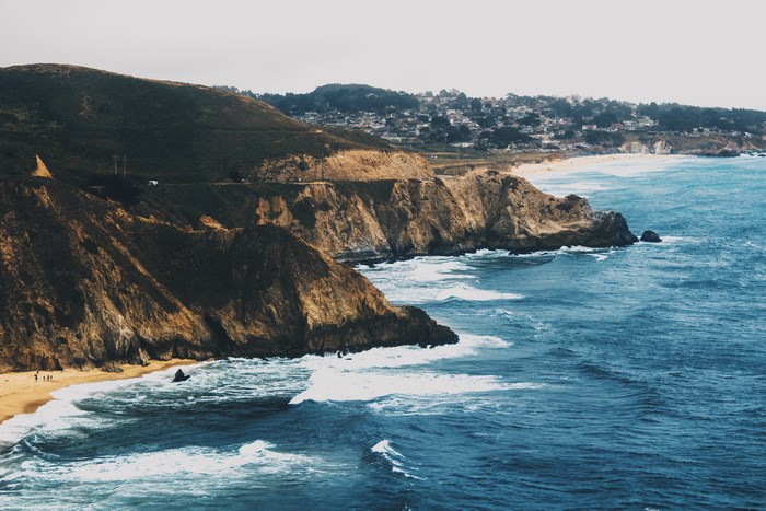 Ocean waves crash against rocky cliffs near a coastal town