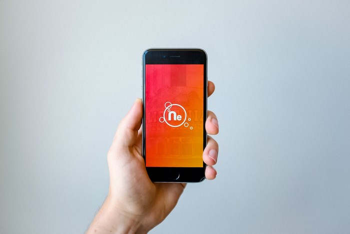 Hand holding iPhone with NE logo and gradient screen