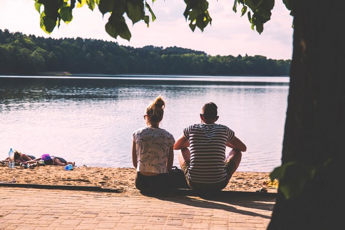 Couple sitting on beach by lake during summer