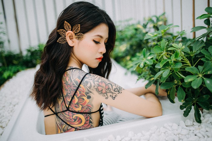 Tattooed Asian woman in bathtub with plants