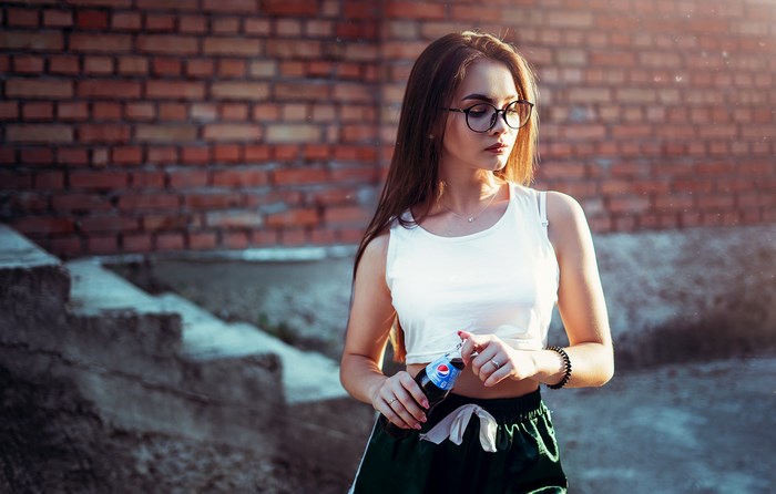 Young woman in glasses holding a Pepsi bottle outdoors