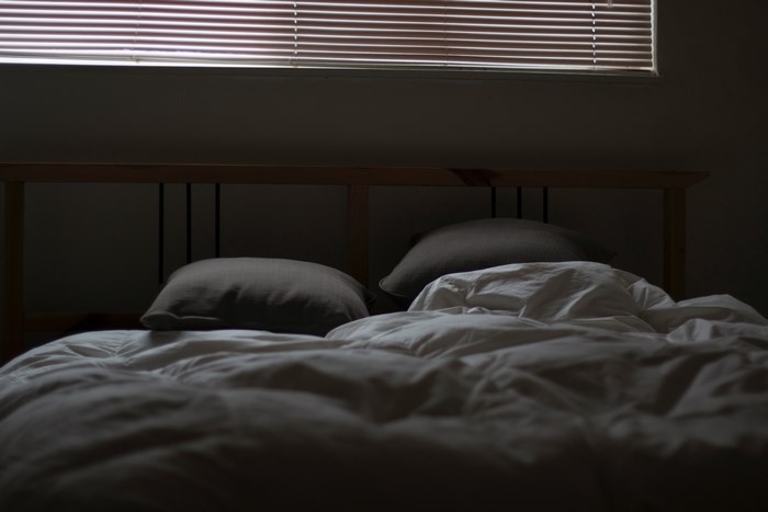 Empty bed with pillows and rumpled sheets near a window with blinds