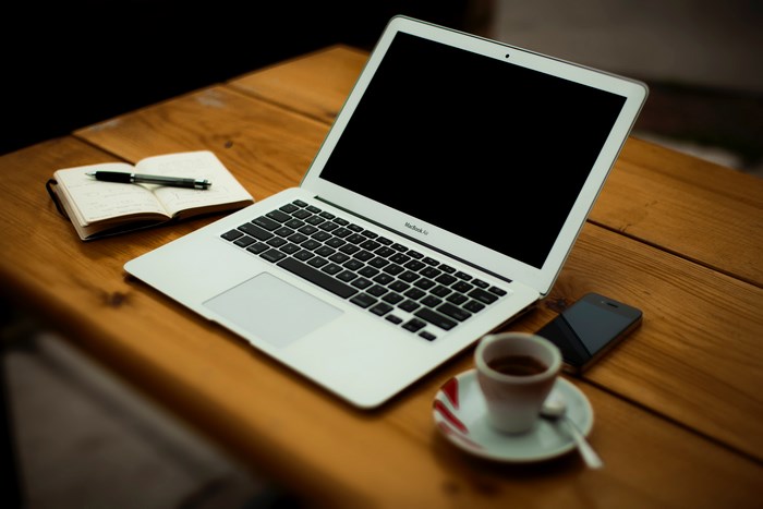 MacBook Air, notebook, pen, phone, and espresso on wooden table