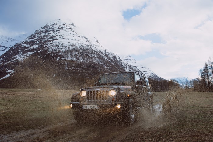 Jeep offroading through mud with snowy mountains in background