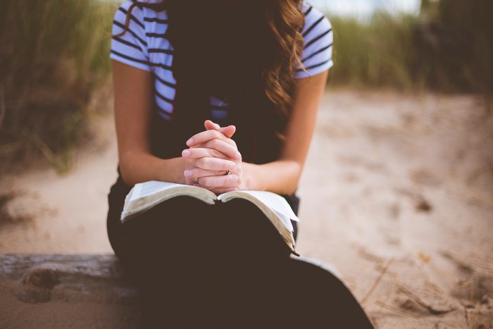 Woman praying with an open book on the sand