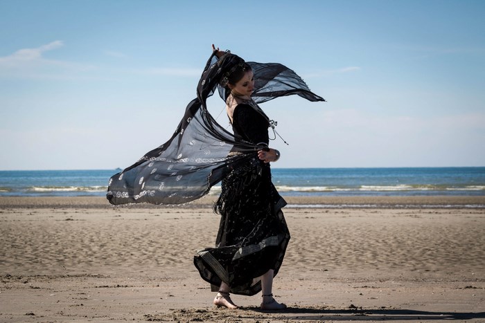 Woman in black dress dancing on a beach with a veil