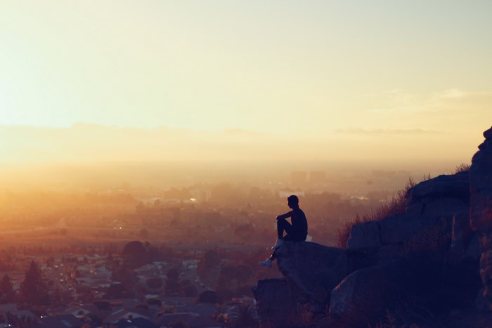 Man sitting on a cliff overlooking a cityscape at sunset