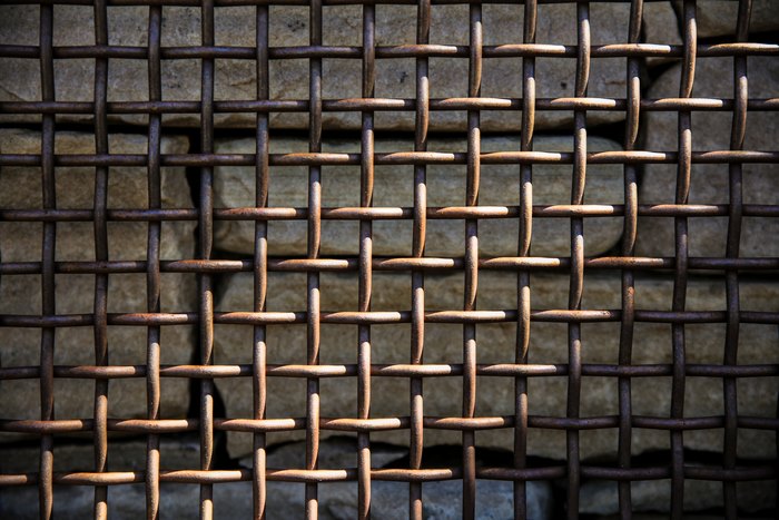 Rusty metal grid in front of stone wall