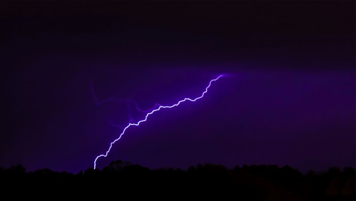 Purple lightning strike over dark landscape