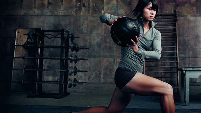 Woman performing medicine ball lunge in gym