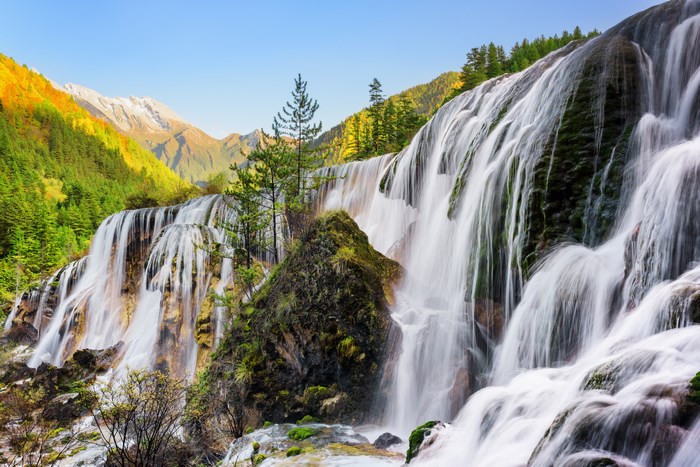 Waterfall cascading down mossy rocks with mountains and forest