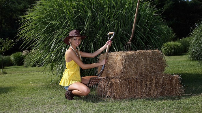 Woman in straw hat with pitchfork and hay bales