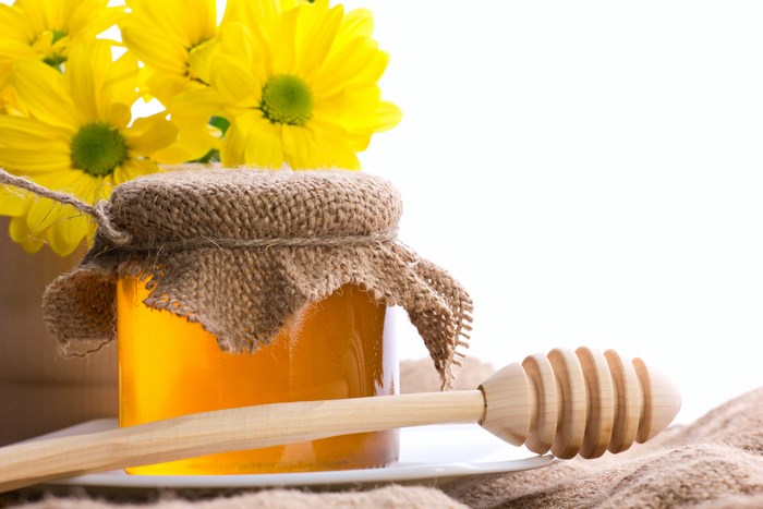 Honey jar with yellow flowers and honey dipper